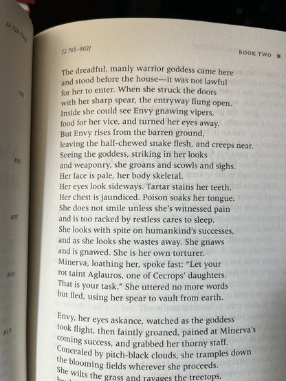 Picture of a book page reading:

The dreadful, manly warrior goddess came here / and stood before the house—it was not lawful  / for her to enter. When she struck the doors / with her sharp spear, the entryway flung open. / Inside she could see Envy gnawing vipers, / food for her vice, and turned her eyes away. / But Envy rises from the barren ground, / leaving the half-chewed snake flesh, and creeps near. / Seeing the goddess, striking in her looks / and weaponry, she groans and scowls and sighs. / Her face is pale, her body skeletal. / Her eyes look sideways. Tartar stains her teeth. / Her chest is jaundiced. Poison soaks her tongue. / She does not smile unless she's witnessed pain / and is too racked by restless cares to sleep. / She looks with spite on humankind's successes, / and as she looks she wastes away. She gnaws / and is gnawed. She is her own torturer. / Minerva, loathing her, spoke fast: "Let your / rot taint Aglauros, one of Cecrops' daughters. / That is your task." She uttered no more words / but fled, using her spear to vault from earth. / Envy, her eyes askance, watched as the goddess / took flight, then faintly groaned, pained at Minerva's / coming success, and grabbed her thorny staff. / Concealed by pitch-black clouds, she tramples down / the blooming fields wherever she proceeds. / She wilts the grass and ravages the treetops