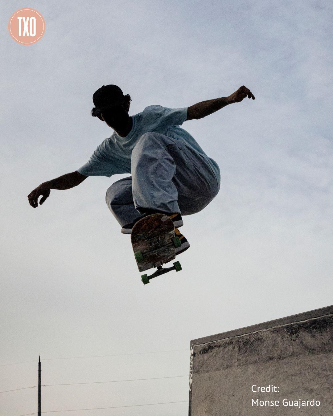 A young man, seen in silhouette, wearing baggy white clothes, takes a seemingly impossibly high jump on his skateboard, seemingly flying over power lines and into the sky with arms outstretched.