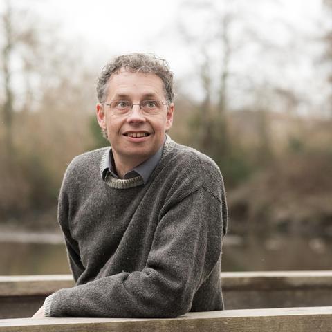Photograph of an attentive scientist wearing glasses and a grey pullover