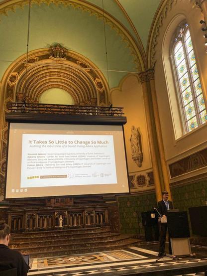 Presenter behind pult in front of slide titled "It Takes So Little to Change So Much", inside a tall church
