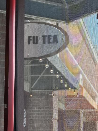 picture taken through a window of a partial sign hanging on the side of a building.  the only letters visible on the sign are

FU TEA