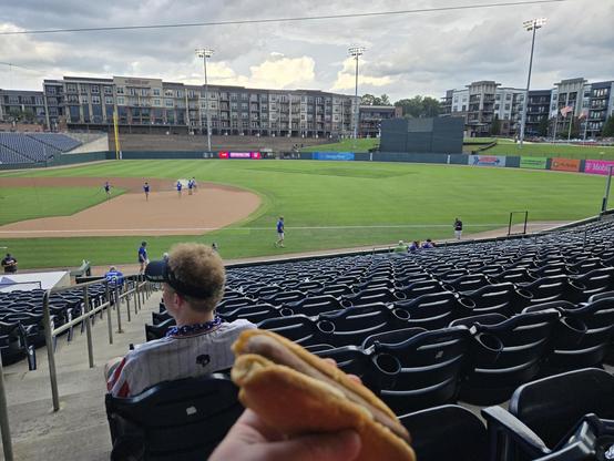 picture of the outfield of a baseball stadium from the first base stands.  an American flag is cut in to the outfield.  a hot dog is visible in the foreground.