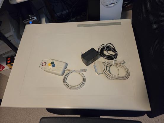 a SummaGraphics SummaSketch II Professional Plus with 4-button pointer, serial cable and power adapter sit on a black rolling chair.