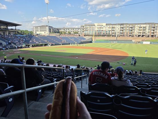 a baseball field nicely prepared with players working out in the outfield.  perspective is from the seats on the first base side.