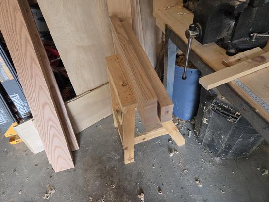 finished stack of 5 legs now 1 7/8" square and 29 1/2" long   the stack is sitting on a wooden a frame stool in front of wood stored vertically.