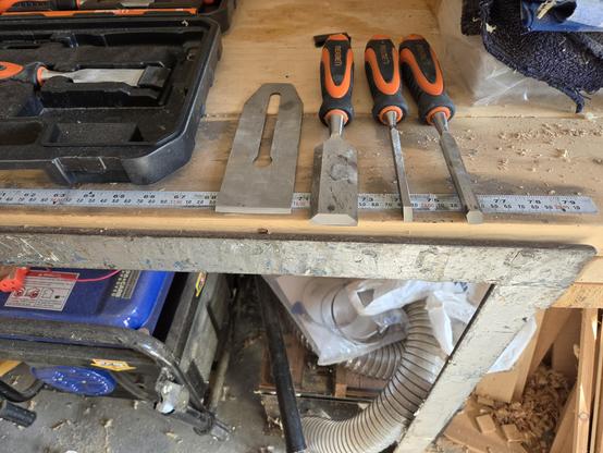 three chisels and a plane iron sitting bevel up on the edge of my workbench.  the tips are shiny and the chisels are (mostly) sharp.