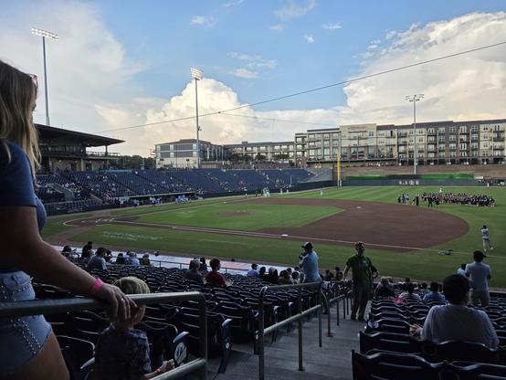 picture of a baseball field from the first base stands.  the infield is empty but there are players warming up and a chorus lined up in the outfield.