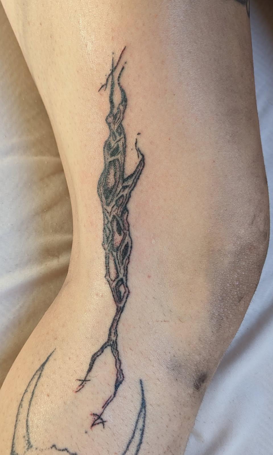 A stylized organic style black handpoked tattoo of a cholla skeleton shard, which looks a bit like a broken branch with holes throughout terminates in sigils at both ends
