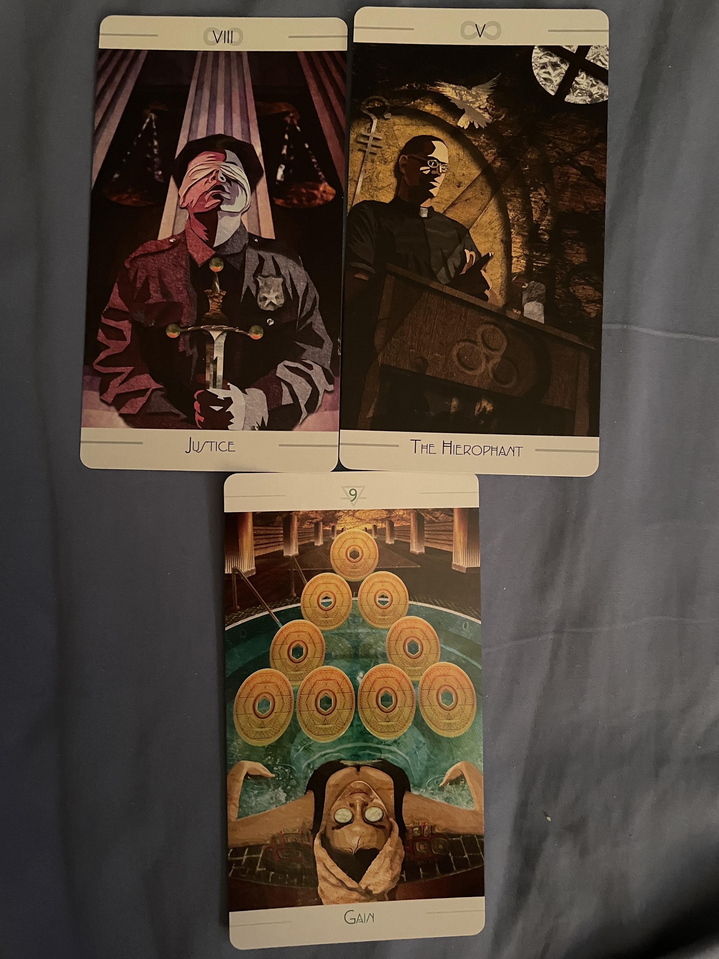 Three tarot cards in an inverted triangle. The top two cards are Justice and the Hierophant, the bottom card is the 9 of Disks.

Justice has a blindfolded, uniformed police officer in front of scales holding a sword by the blade. The Hierophant shows a monster in the pulpit, a cutout of a dove above him. The Nine of Disks shows a woman relaxing in a spa, cucumber slices over her eyes, with nine coins in a pyramid in front of her.