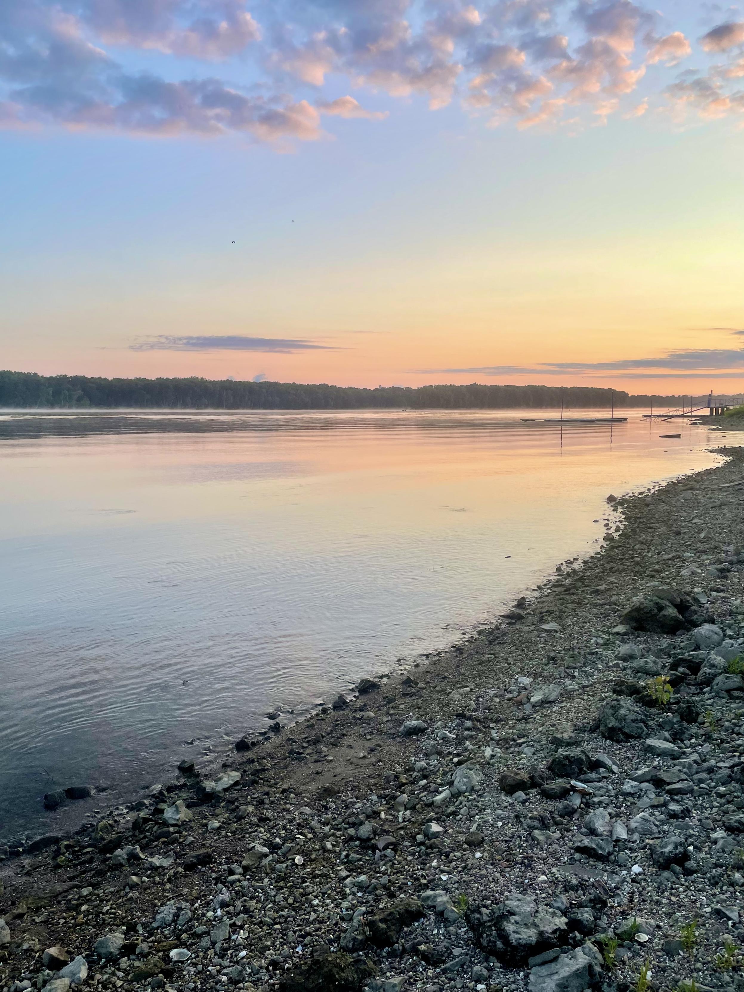 sunrise reflecting on the river, some small cotton ball clouds high up in the sky
