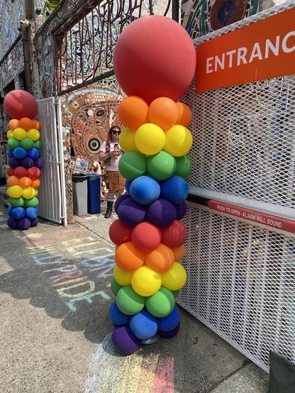 The entrance to the Magic Gardens on Philadelphia's South STreet: a metal set of gates are opened back, allowing entrance to the heavily mosaic-laden walls within.  In front of the gates are two vertical columns of balloons in a repeating rainbow of shades, each topped with a really humongous red balloon.  Between the columns, not noticed by me at the time, is rainbow chalk spelling out Celebrate Philly Pride.