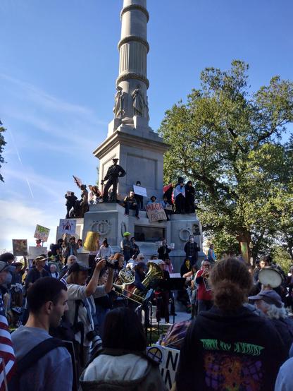 Picture showing more of the column the band is playing at the base of. Several people have climbed up the column.