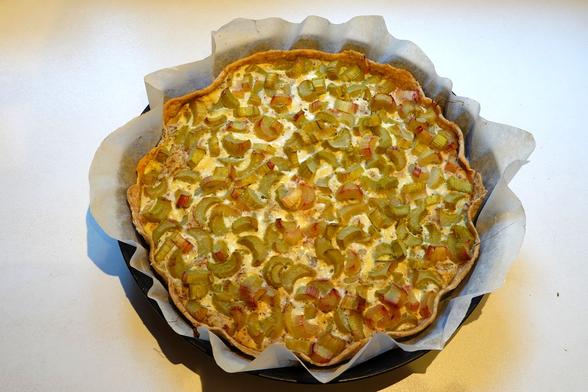 Rundes Kuchenblech mit frisch gebackenem Rhabarber-Kuchen (noch heiss) auf weissem Hintergrund