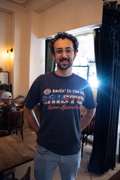 Un homme qui pose pour la caméra, étant debout, avec une sourire, et son t-shirt dis « Racin’ in the USA. Bristol. NASCAR Speedway. »