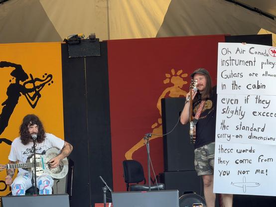 Dug on stage and one member is holding up a long sign that reads:

Oh Air Canada
Instrument policy
Guitars are allowed
In the cabin
Even if they
Slightly exceed
The standard
Carry-on dimensions
These words
They come from
You not me!