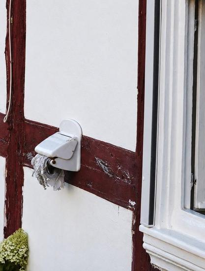 An der Außenwand eines Hauses hängt ein Klorollenhalter aus Porzellan. Die Witterung hat die Klorolle im Laufe der Zeit ziemlich zerfetzt.