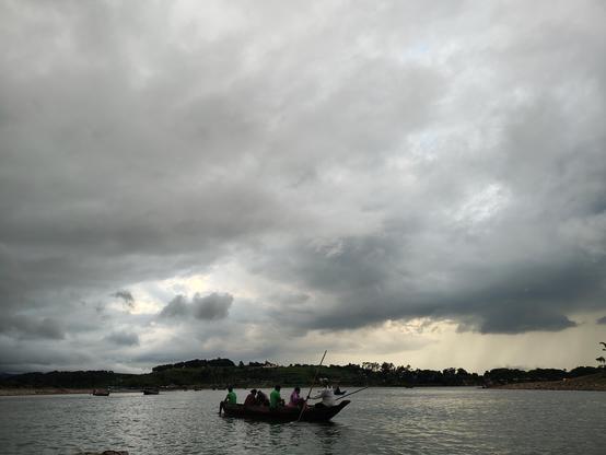Photography showing a river, a boat full of people and trees on the other side