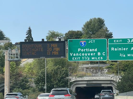 Freeway signs above a tunnel entrance. There's a digital sign that gives time estimates reading:

Downtown    3 min
Northgate    20 min
Seatac       13 min