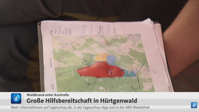Screenshot aus dem tagesschau-Beitrag "Brand in Hürtgenwald: Freiwillige unterstützen Löscharbeiten" vom 16.08.2026.

Zu sehen ist ein Klemmbrett mit dem Ausdruck einer Karte, welche vom Kartenstil recht eindeutig als OpenStreetMap einzuordnen ist.

Auf dem Ausdruck ist ein größeres Gebiet tiefrot markiert, daneben zwei kleinere mit Gelb und Hellblau.

Handschriftlich wurden zahlreiche Anmerkungen und Linien mit Kugelschreiber hinzugefügt.