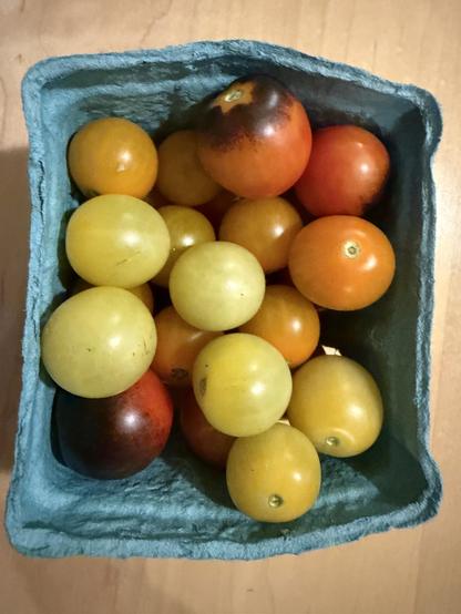 A small green cardboard box full of cherry tomatoes of different types.