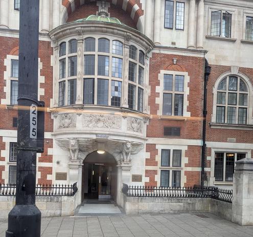 Red brick and light coloured stone doorway with arched entrance. Carvings along and above. Bow window projecting above door.