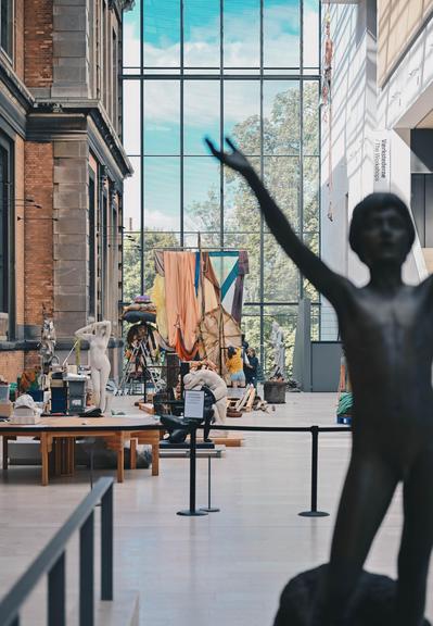 Kunstværker under installation i stort museumsrum. Mørk skulptur i forgrunden.