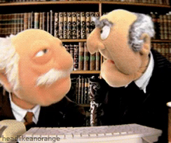 The muppets Statler and Waldorf looking into a screen and laughing uproariously.