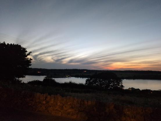 A sunset across a body of water, the Menai Strait with streaks of cloud like mares' tails lit orange by the setting sun.