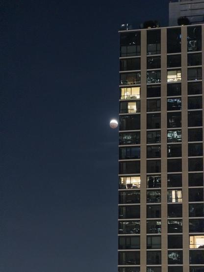the moon, at about 75% eclipsed, kissing an apartment building