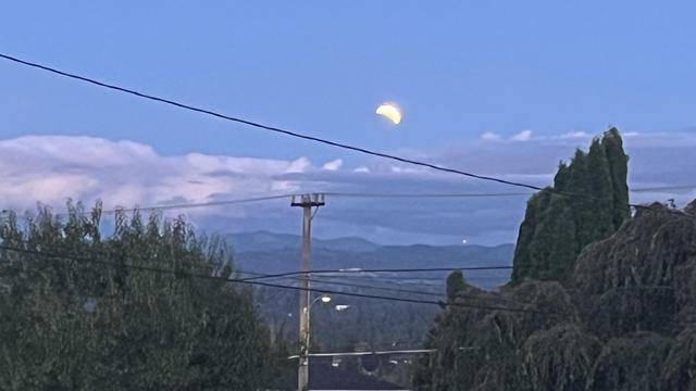 A view to the southeast. The sky still has lots of blue in the evening. There are low clouds on the horizon but the full moon hangs above them. The Earth’s shadow obscures the moon’s lower left quadrant.