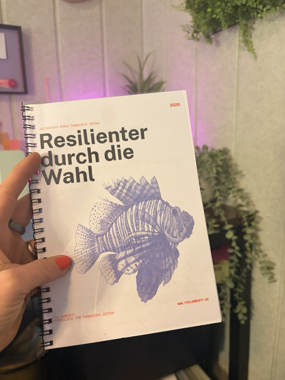 Workbook vor Wand in der Hand. Titel mit Fisch.