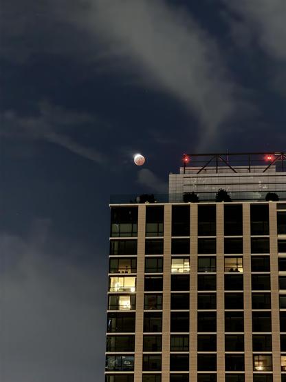 The moon, about 95% eclipsed - a bright sliver at the top fading into a reddened bottom - sailing over the Perla building in downtown Los Angeles.