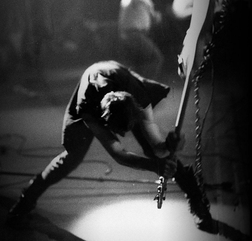 Ein Mann zerschmettert einen E-Guitarre auf einer Musikbühne. 
Das Iconografische Bild von The Clash London Calling