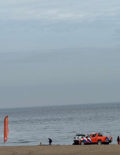Blick auf etwas Strand, Meer und viel Himmel. Am Ufer findet eine Übung der Seenotrettung statt.