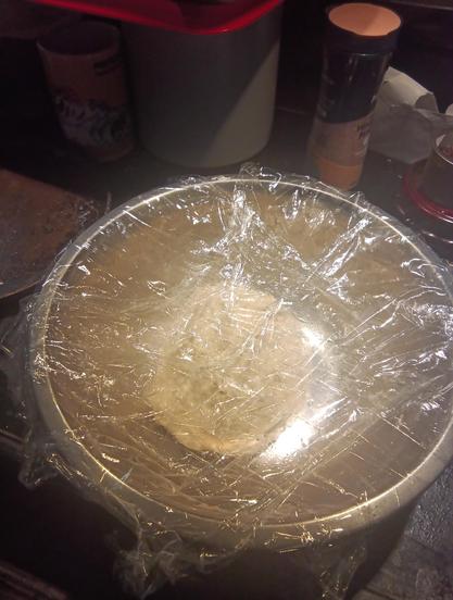 dough ball in a metal mixing bowl, covered in plastic wrap