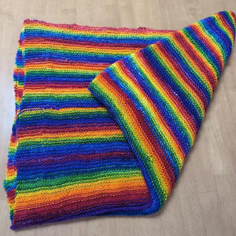 Photo of a beautiful, hand knitted throw in vibrant rainbow colors. What the photo can not convey is the softness and springiness of the merino wool yarn from which it is made.