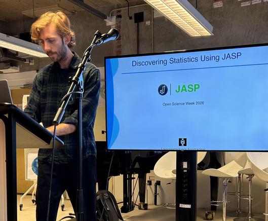 Johnny van Doorn in front of a screen with a slide on it and the text “Discovering statistics using JASP”.