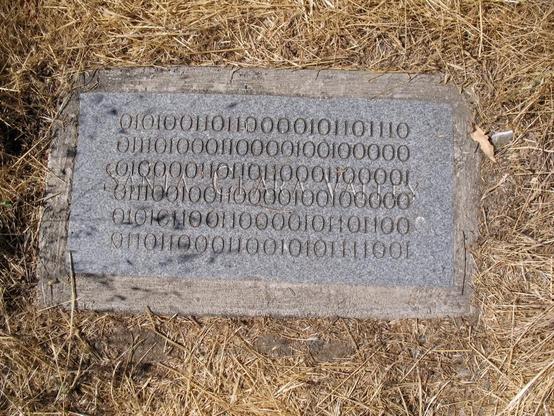 A concrete plaque with engraved ones and zeroes sits flush in the ground surrounded by dry grass. It also is engraved with SANTA CLARA VALLEY.