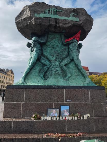 Skulpturen Arbetets ära. 
Vid foten ser vi foton, blommor och levande ljus.