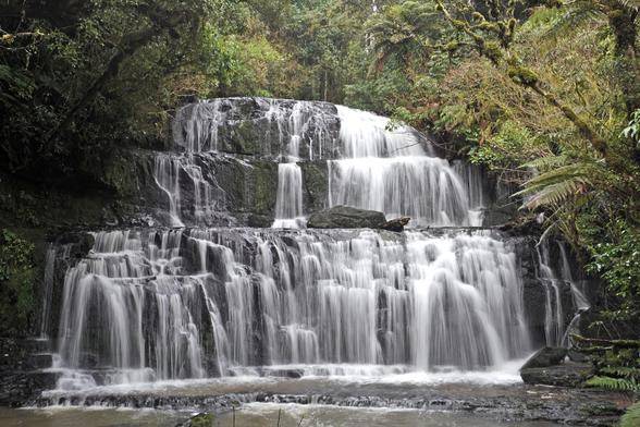 A three-tiered waterfall in a forest. Three is the main number of tiers, but the lowest tier has a lot of small waterfalls inside it.