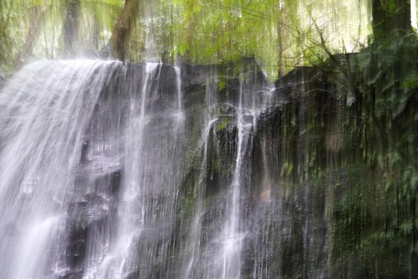 Detail behind a waterfall. This is a long exposure so the water looks like white streams going straight down. There is also some green cliffy rock to the right of the picture.