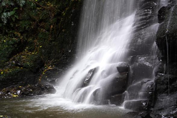 A different waterfall with water falling straight down and also water running over a slab of dark gray rock.
