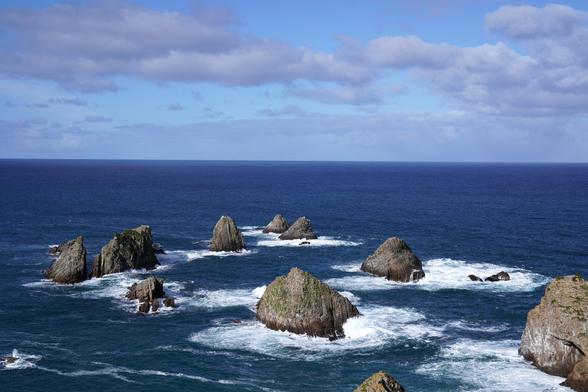 Another shot of the near-shore at Nugget Point, with dark blue water, waves, and a couple of rocks peeking up.