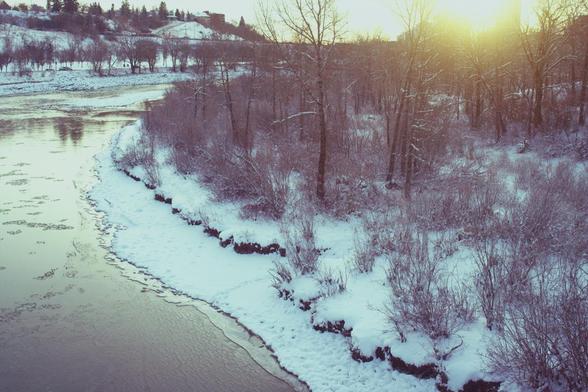 Sunrise over a frozen river. Some bare trees form a little woods.