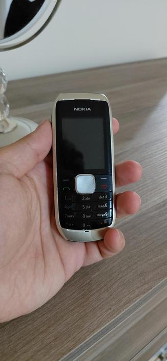 an old nokia phone from mid 2000s in my hand. it's small and got buttons. sixteen plus a keypad to be exact