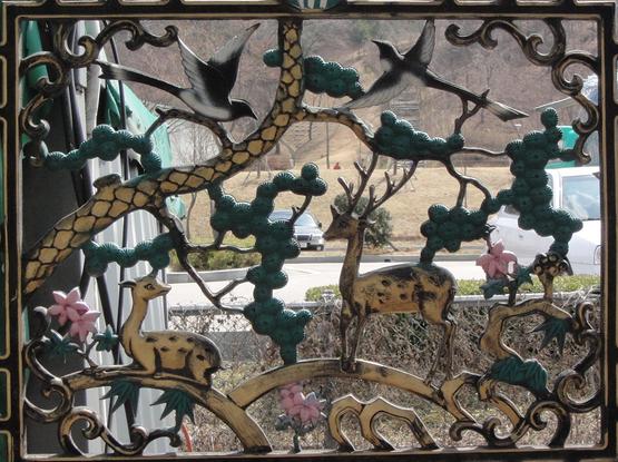 A decorative panel within a window features a tree branch with birds, a deer, and a small animal. The design includes flowers and intricate details, creating a natural scene.
Auf einer in ein Fenster eingesetzte Zierplatte sind ein Ast mit Vögeln, ein Reh und ein kleines Tier abgebildet. Das Motiv enthält Blumen und filigrane Details, die eine naturgetreue Szene ergeben.