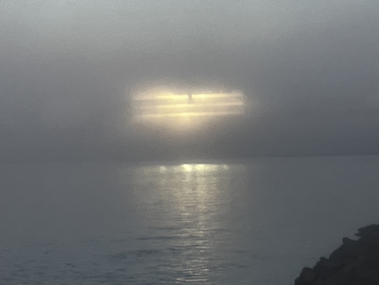 A building along the beach reflecting the setting sun back on the water through the fog.