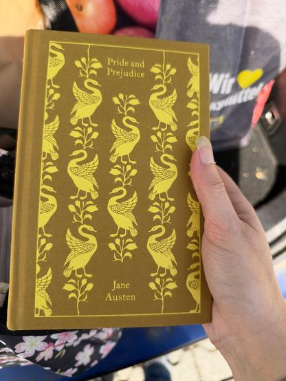 A bound edition of a book with Pride and Prejudice stamped on the front. It has swans or similar in bright yellow on a curry yellow textile all over it