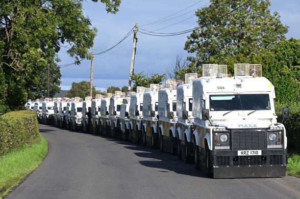 A line of what must be 20 RUC armoured land rovers parked in a small road just outside Portadown. The Land Rovers are white, and covered in metal cages at various weak points.