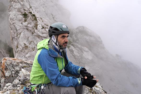 Another person, also wearing a helmet, ponders the situation. Some rocky features visible behind, but not good visibility.